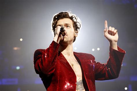 Singer in a red sequined jacket performing onstage with a microphone and one hand raised beneath bright concert lights.